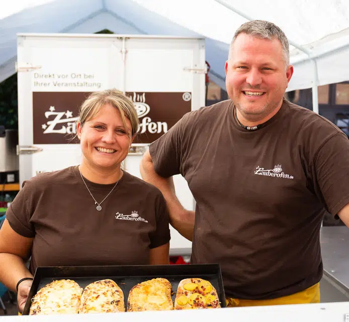 Die Inhaber von Zauberofen mit frisch zubereiteten Speisen vor dem mobilen Ofen.